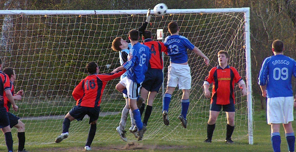 The overworked Times Inn goalkeeper claws at the ball as Smith and Campbell attack.